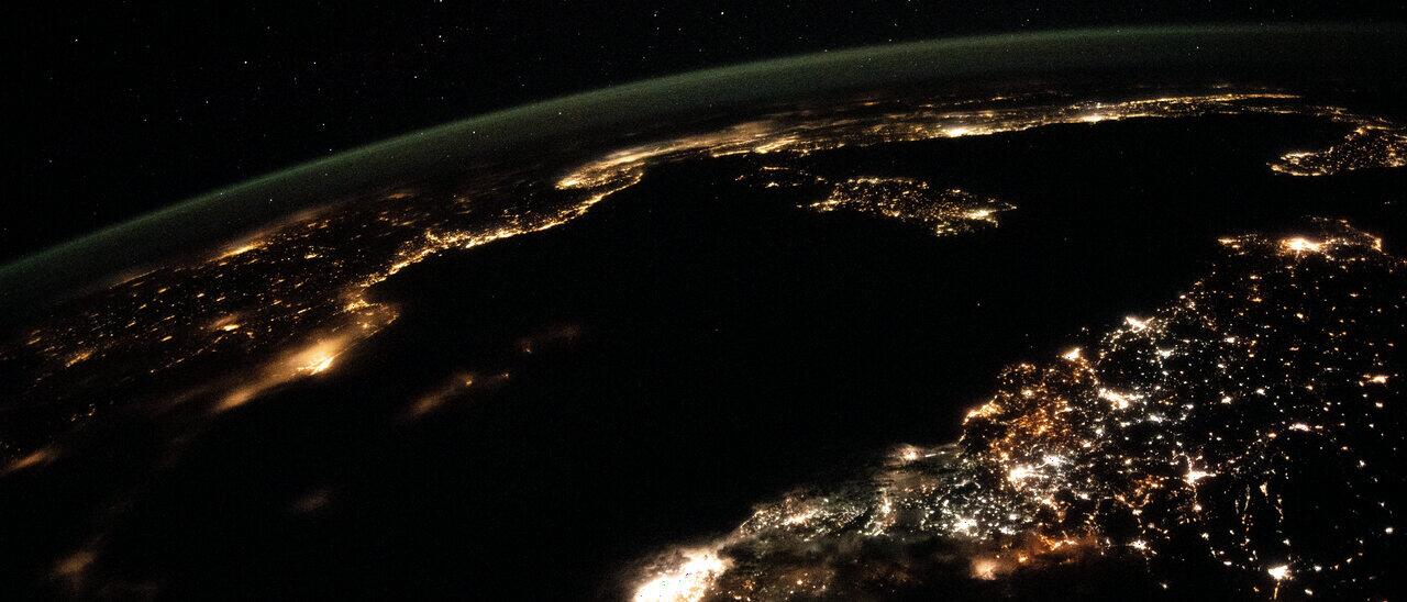 Northern Europe at night from orbit, city lights along the coastlines beneath an aurora